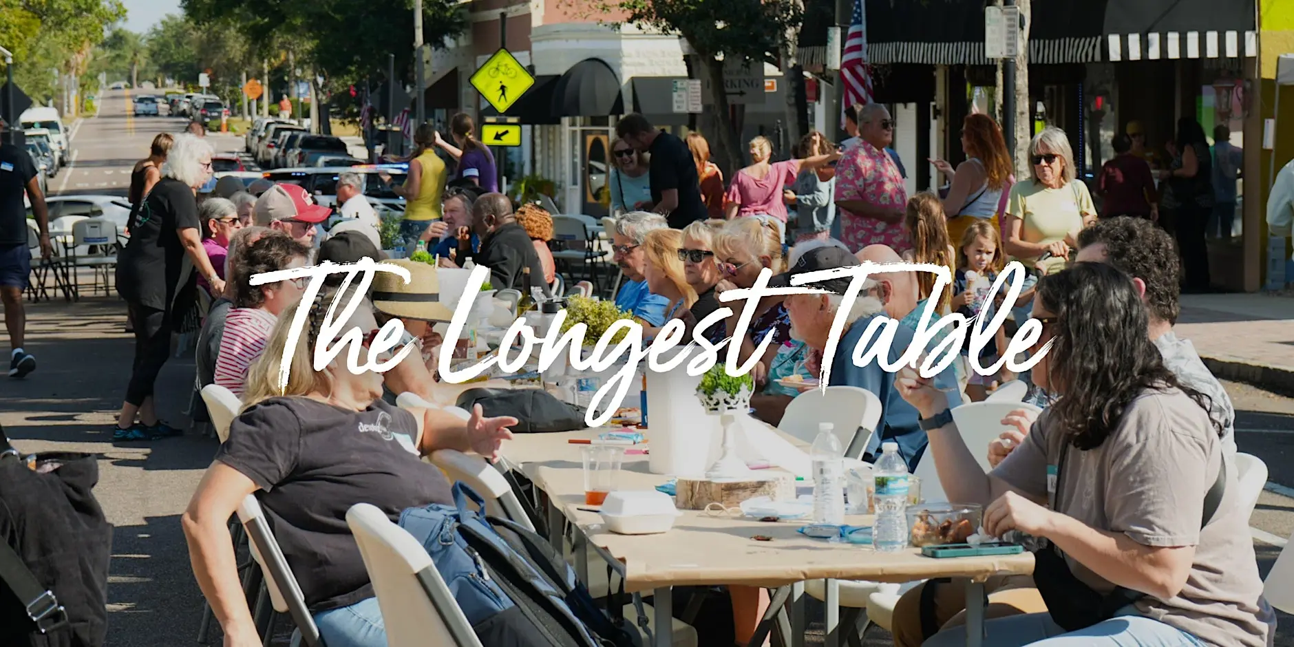 Neighbors filling one long table down a sunny downtown street at a Longest Table community event